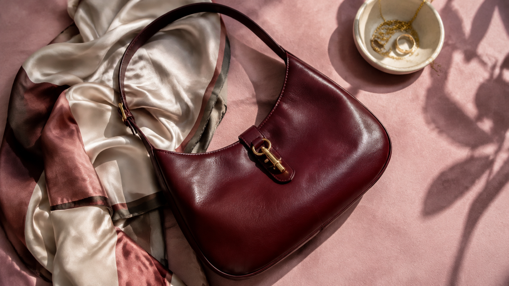 Borsa a spalla senza marchi in pelle bordeaux su tessuto rosa con un foulard